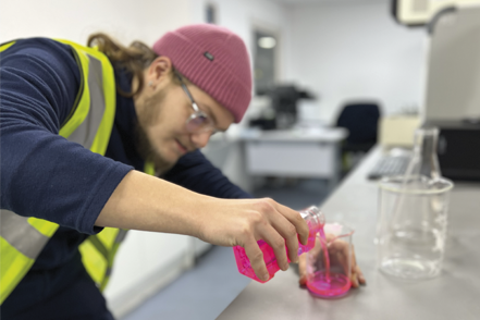 lab worker pours chemicals into a container during the creation of a new product